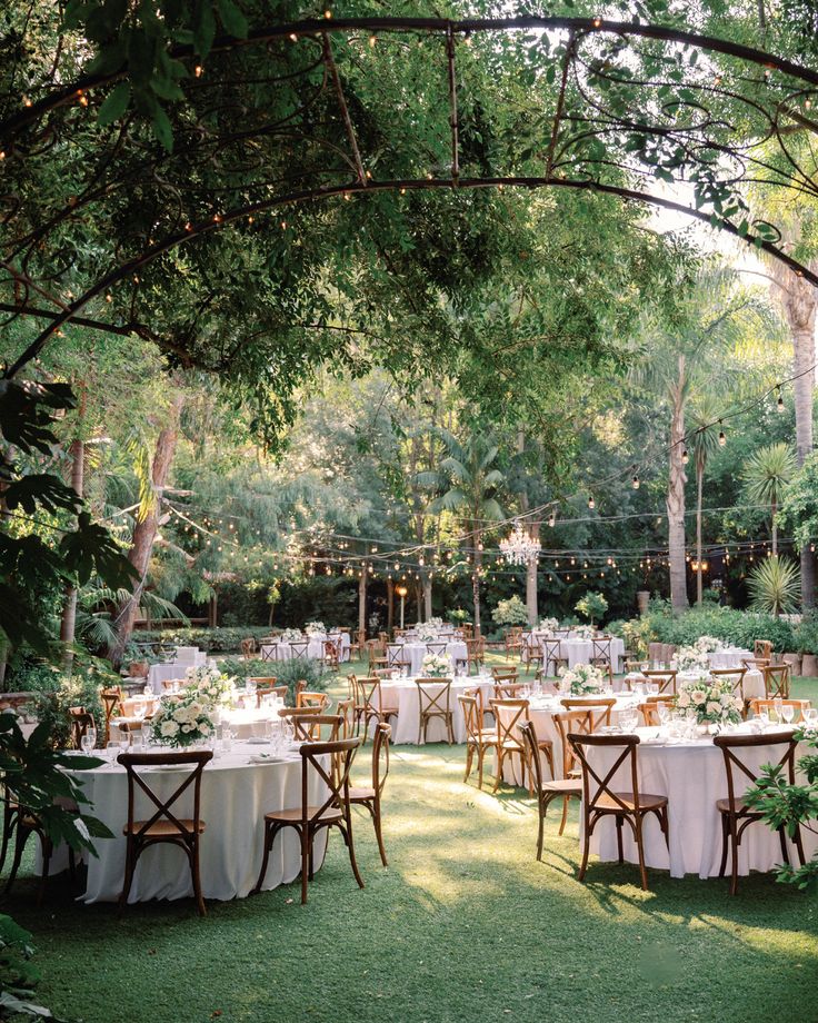 an outdoor wedding reception set up with tables and chairs in the middle of a garden