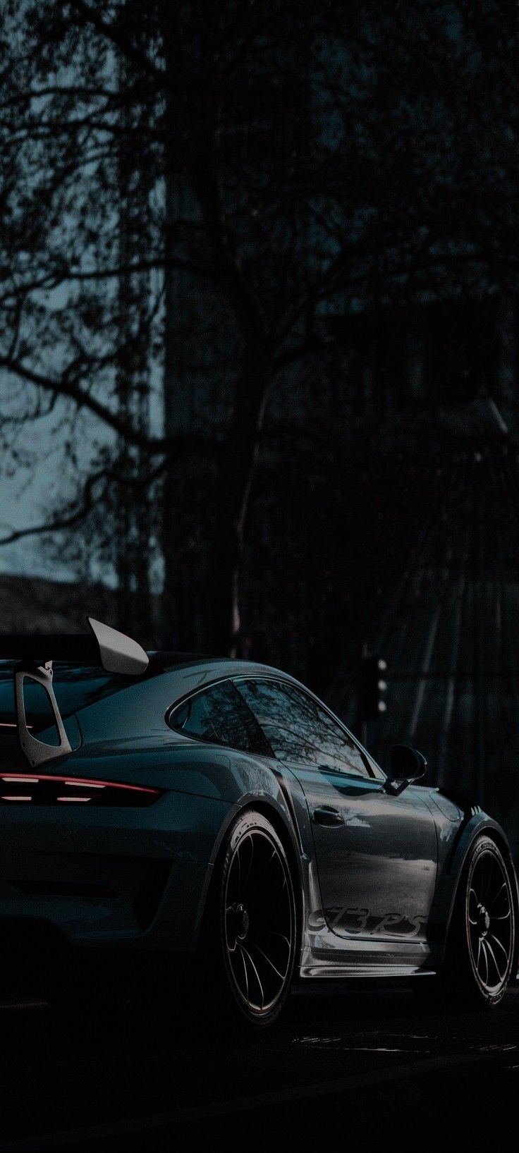 a black porsche sports car parked on the side of the road at night with trees in the background