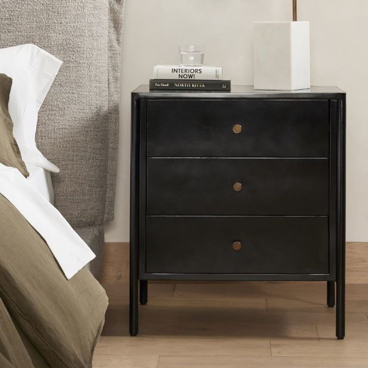 a night stand with two books on top of it next to a bed and nightstand