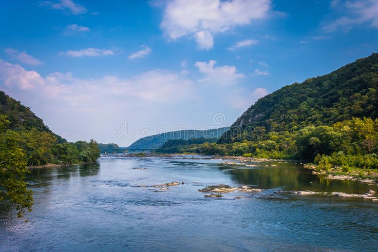 a river surrounded by trees and mountains under a blue sky with clouds stock photos - image