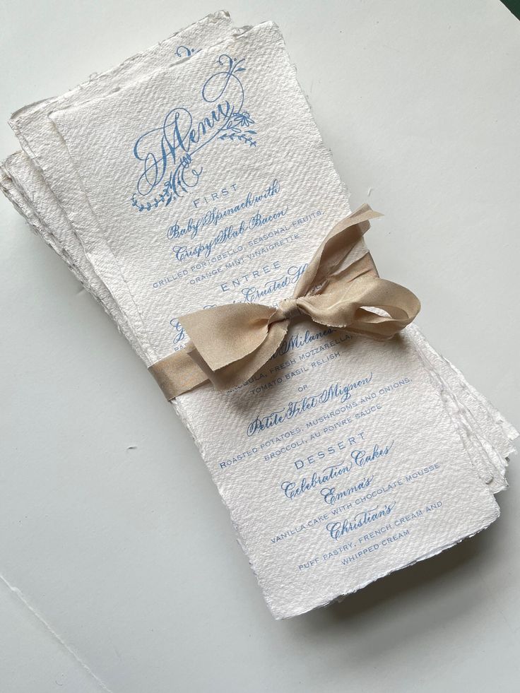 a white and blue wedding card with a brown bow on the front is sitting on a table