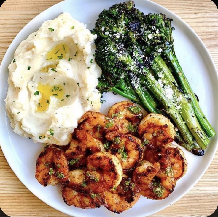 a white plate topped with shrimp, mashed potatoes and broccoli