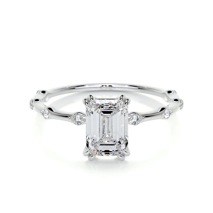 an emerald cut diamond engagement ring with diamonds on the band and shoulders, set in 18k white gold