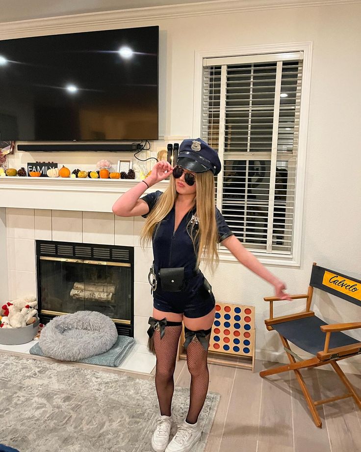 a woman in short shorts and a hat standing next to a fire place with her hands on her hips