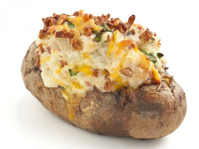 a baked potato with cheese and other toppings sitting on a white surface, ready to be eaten