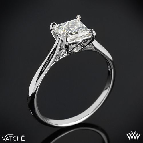 a white gold ring with a princess cut diamond in the center on a black background