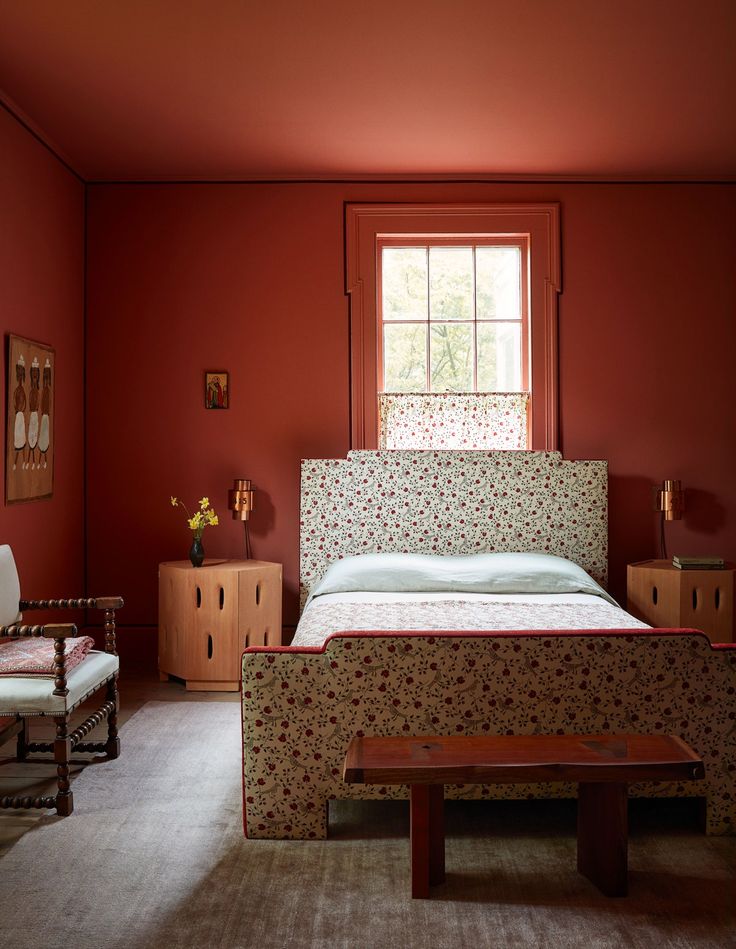 a bed sitting in the middle of a bedroom next to a chair and window with red walls