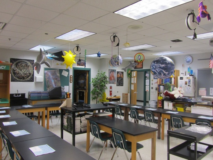 an empty classroom with desks, chairs and pictures hanging from the ceiling on the walls