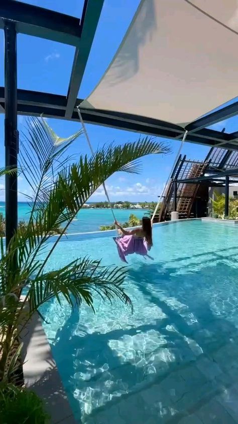 a woman in a pink shirt is floating in a pool with palm trees and blue water