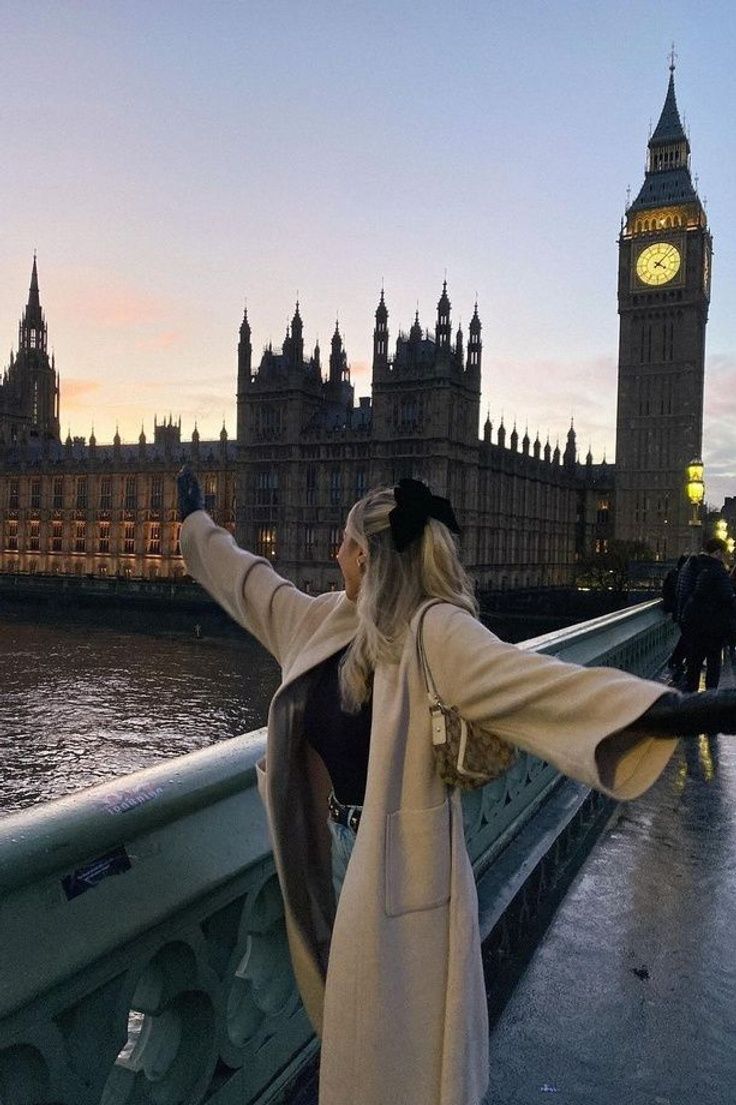 a woman standing in front of the big ben clock tower with her arms spread out