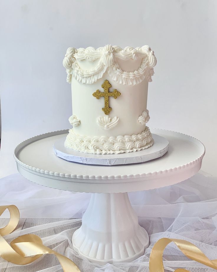 a white cake with a cross on it sitting on top of a table next to gold ribbons