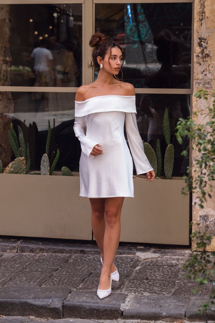 a woman in a white dress is walking down the street with her hand on her hip