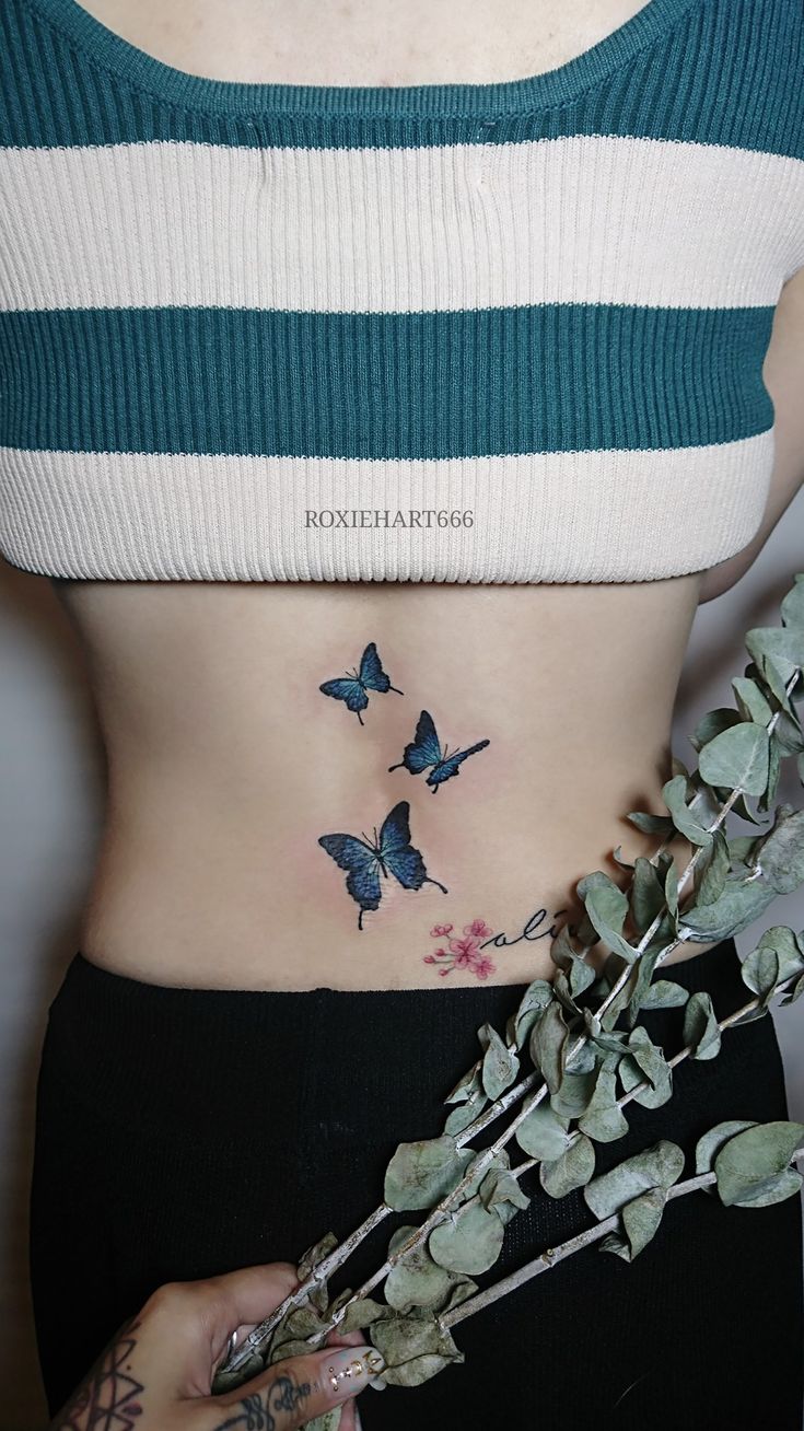 a woman's stomach with three butterflies on her side and flowers in the foreground