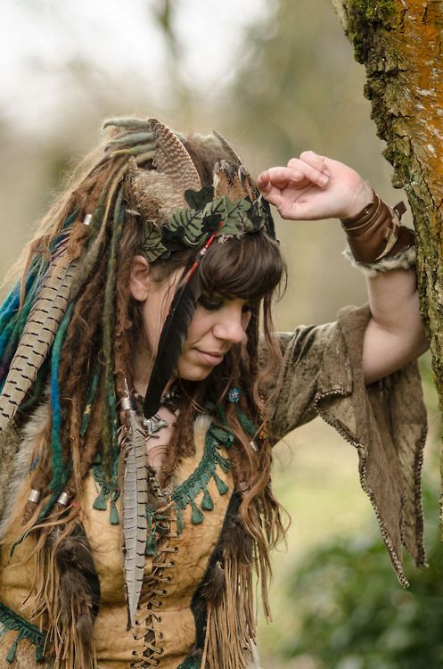 a woman with dreadlocks is standing next to a tree and holding her hand on her head