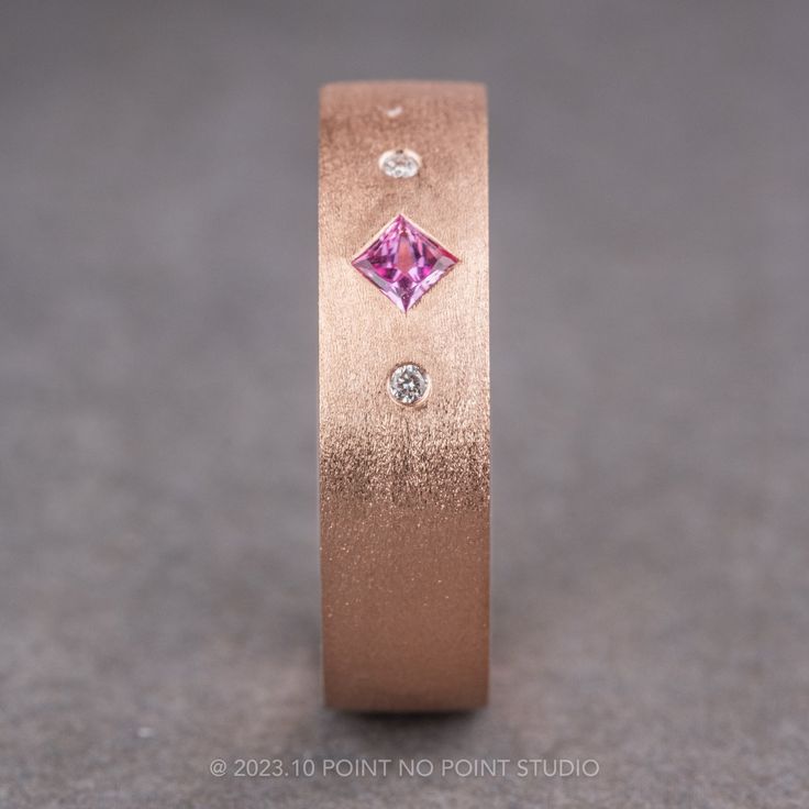 a pink diamond ring with three diamonds on it's side, in front of a gray background