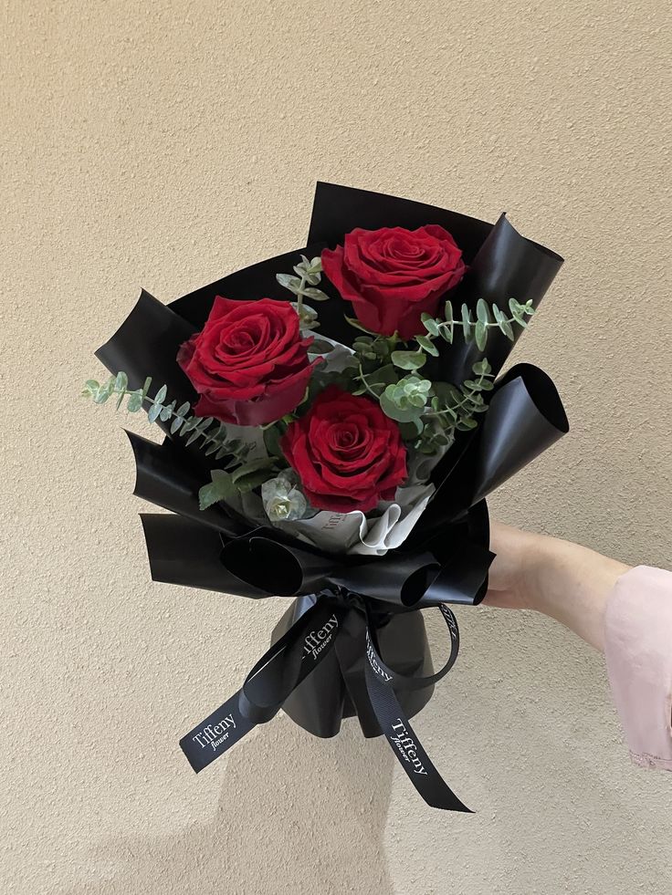 a person holding a bunch of red roses in their hand with ribbon around the bouquet