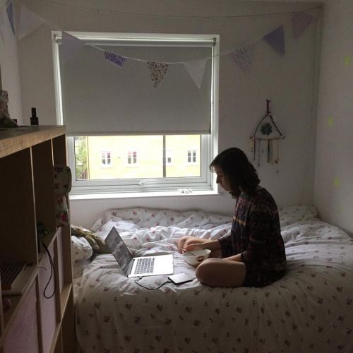 a person sitting on a bed with a laptop in front of them and a window