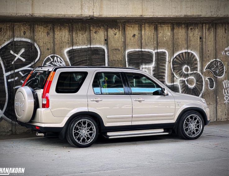 a white suv parked in front of a wall with graffiti on it's side