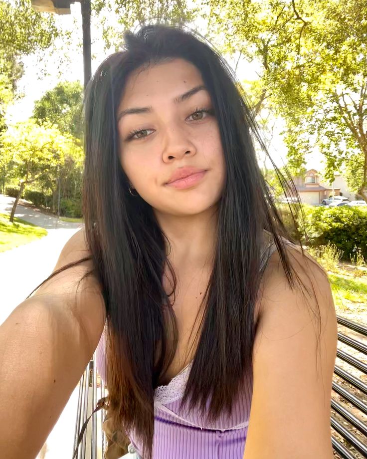 a young woman sitting on top of a wooden bench next to a park area with trees in the background