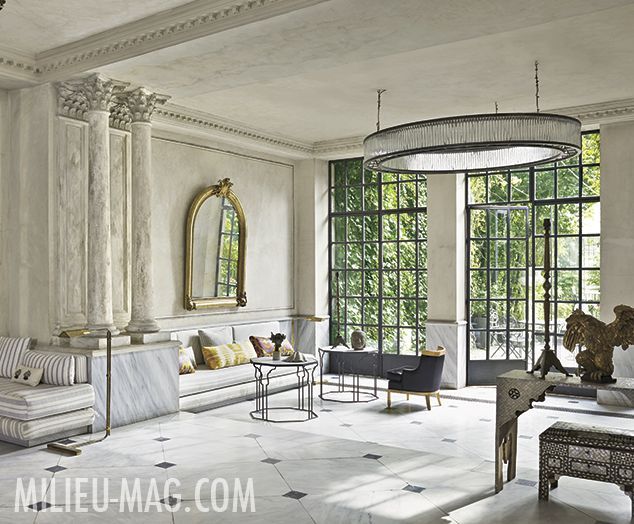 a living room filled with lots of furniture next to tall windows on the side of a wall