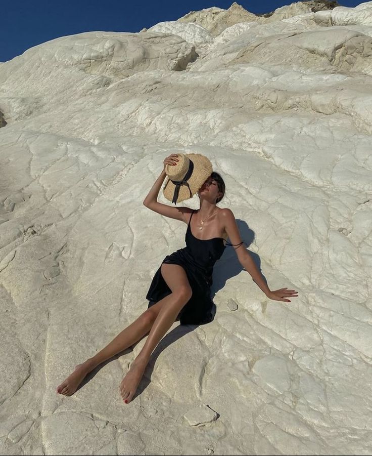 a woman in a black dress and hat laying on top of a large white rock