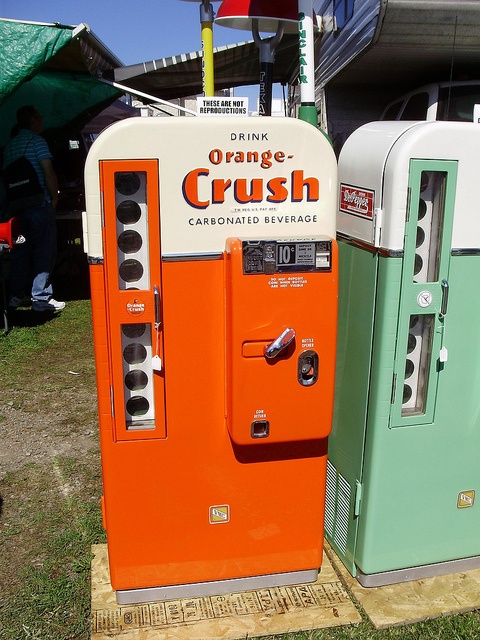 two vending machines sitting next to each other on top of a grass covered field