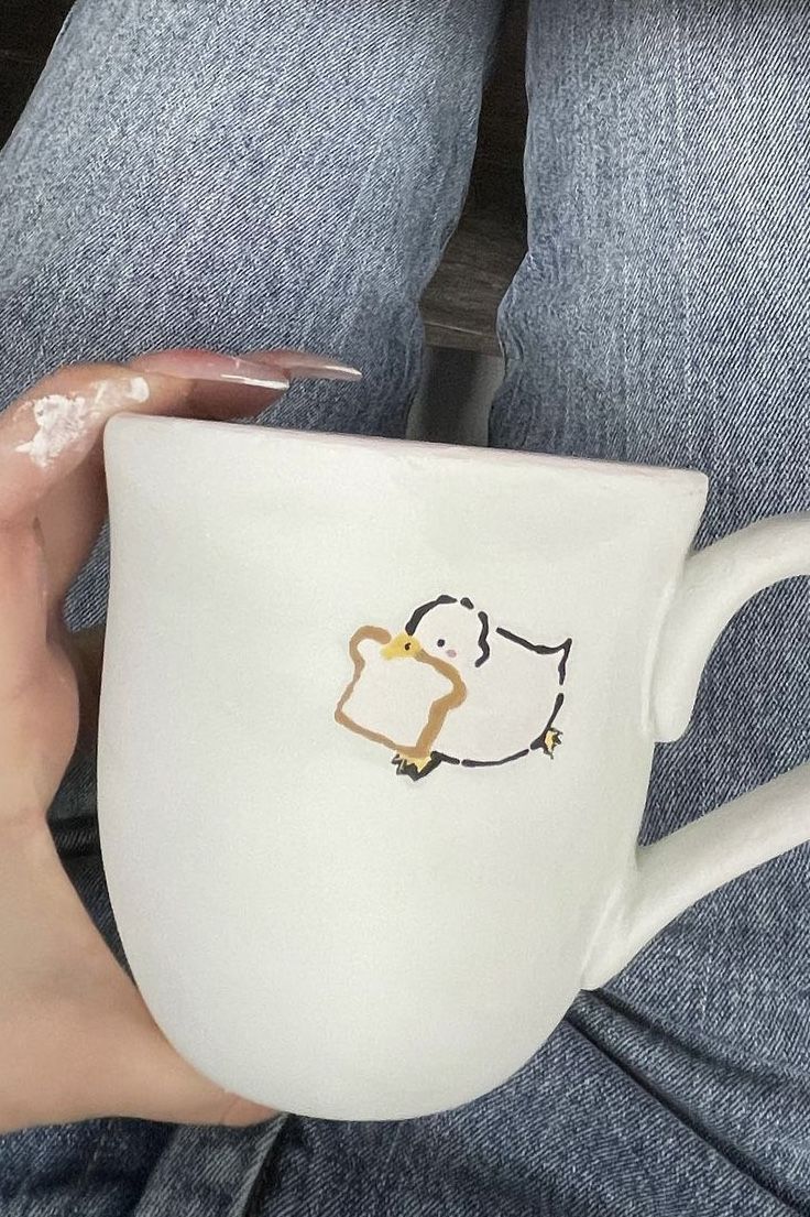 a person holding a white coffee cup with an animal drawn on the side and gold trimmings