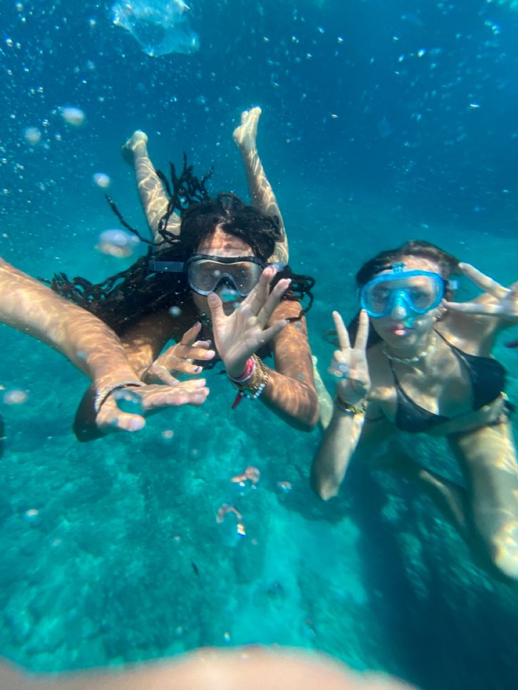 two people are swimming in the water with their hands up and one person is wearing goggles