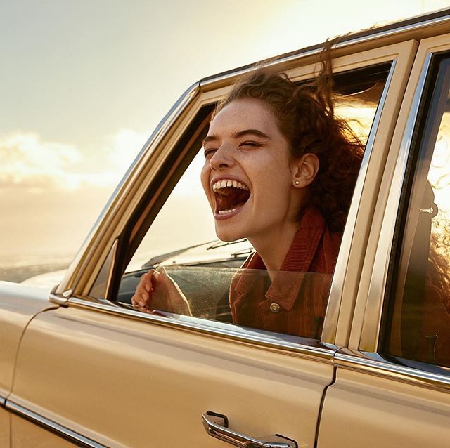 a woman laughing in the back seat of a car with her head out the window