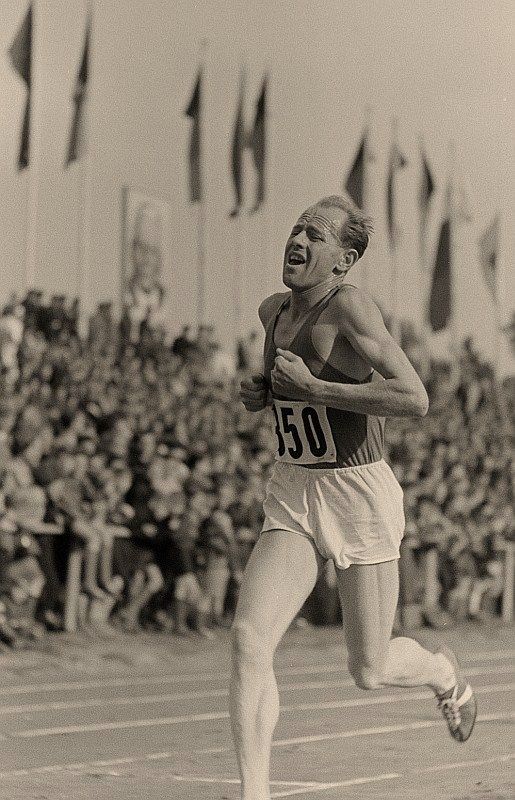 an old photo of a man running on a track in front of a large crowd