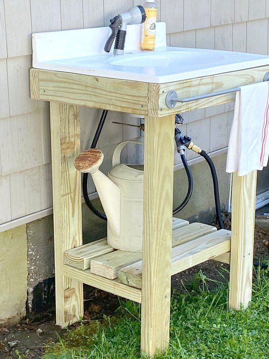 a sink in the grass next to a building with a towel hanging from it's rack