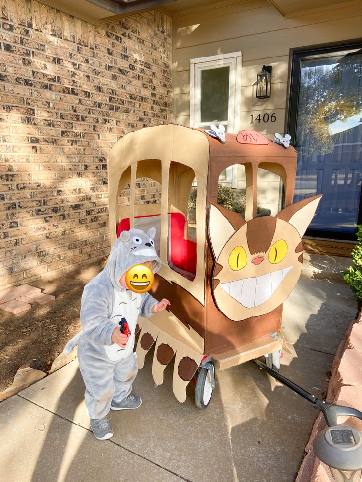 a child in a costume standing next to a toy train with a cat on it