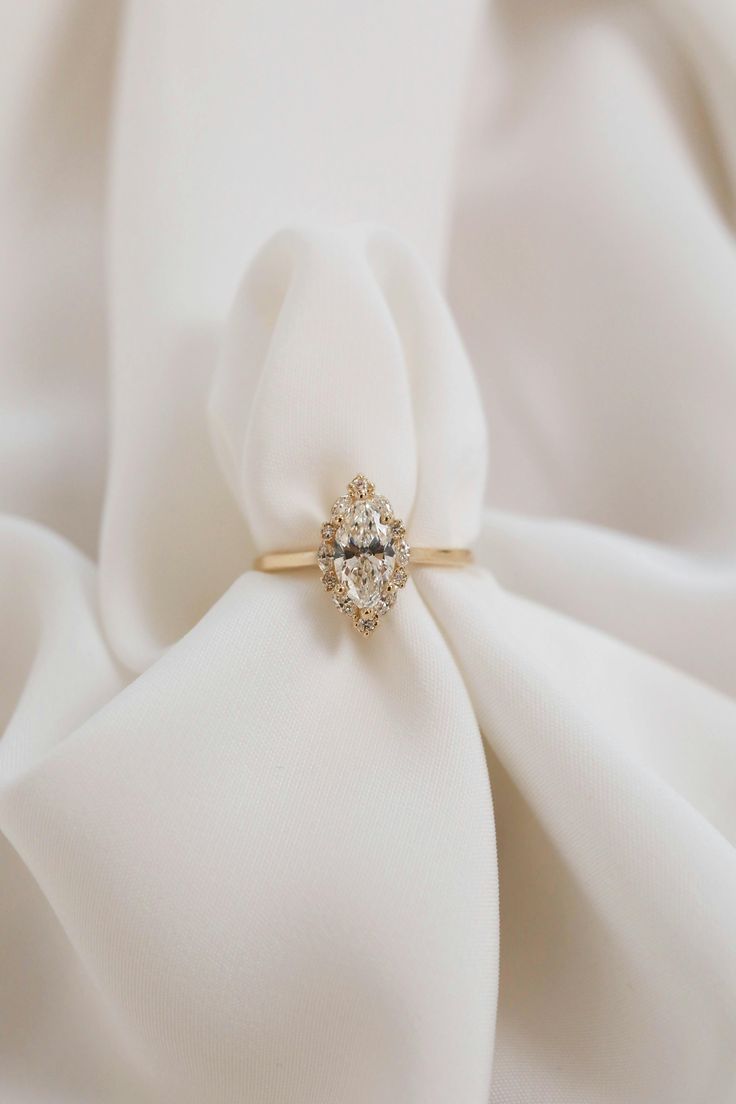 a diamond ring sitting on top of a white satin material with a bow in the middle