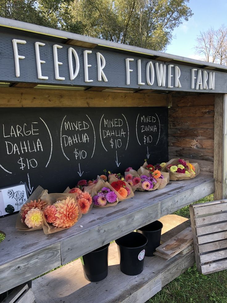 flowers are laid out on a bench in front of a flower farm sign and buckets