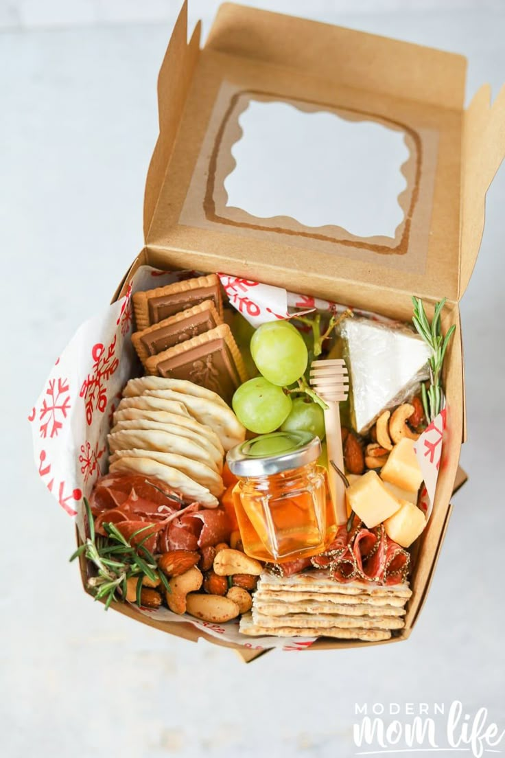 an open box filled with cheese, crackers and nuts next to a bottle of wine