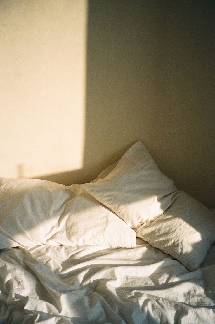 an unmade bed with white sheets and pillows in a room that is light colored