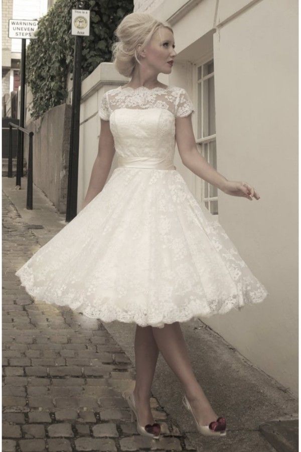 a woman in a short white dress standing on the sidewalk with her hands out to the side