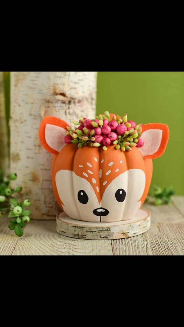 an orange and white pumpkin decorated like a fox with flowers on its head sitting next to a tree