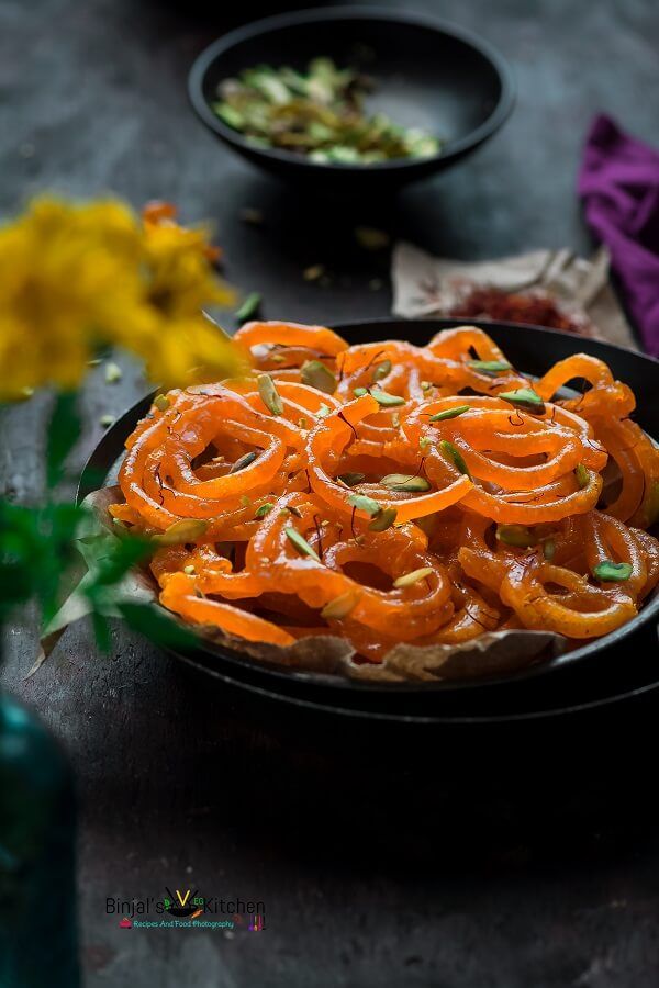 a black plate topped with sliced carrots next to a vase filled with yellow flowers