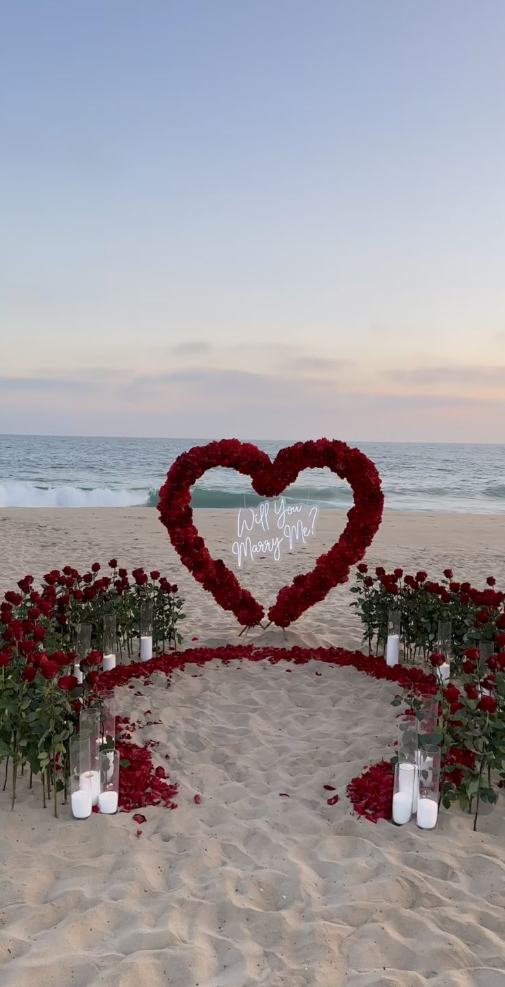 a heart shaped arrangement on the beach with candles