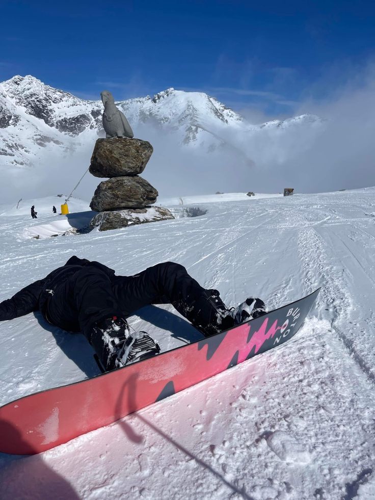 a snowboarder laying on his back in the snow with mountains in the background