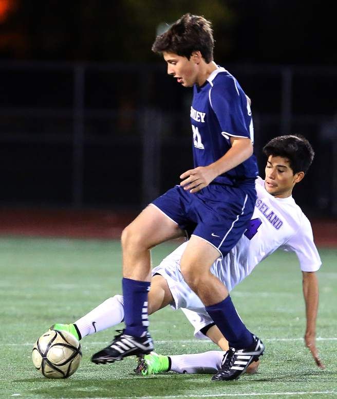 two young men playing soccer against each other on a field with lights in the background