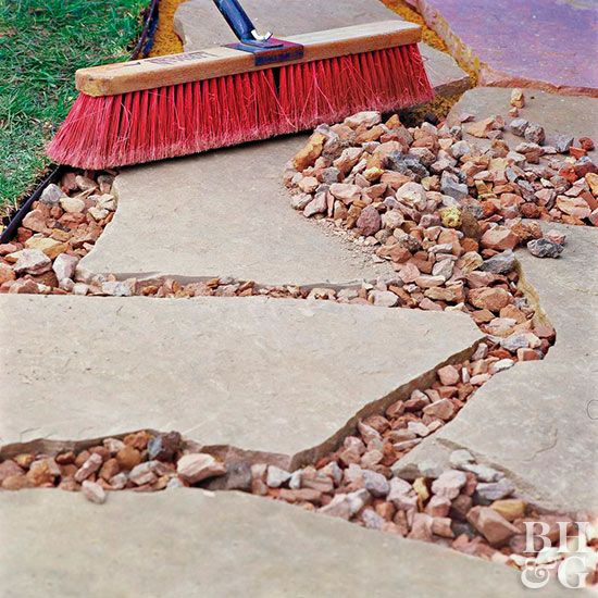 a red broom sitting on top of a sidewalk next to a pile of rocks and grass