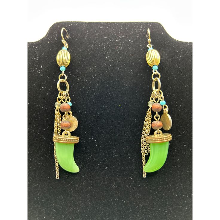 These earrings feature a bohemian tribal design, combining the elegance of gold chains, earthy beads, and a striking green horn charm. Their unique and eclectic style tells a story of adventure and wanderlust, making them a conversation starter and a statement piece in your jewelry collection. Let these earrings take you on a journey every time you wear them. * Boho tribal design * Dangle style * Green horn charm * Gold chains * Earthy beads * 3.25" long * Hook closures top to bottom = 3.25 inch Bohemian Gold Earrings With Beaded Chain, Bohemian Bronze Jewelry With Dangling Beads, Green Dangle Chandelier Earrings With Latkans, Green Bohemian Chandelier Earrings With Dangling Beads, Green Bohemian Metal Chandelier Earrings, Green Bohemian Chandelier Earrings, Green Metal Bohemian Chandelier Earrings, Green Dangling Charms Jewelry, Nickel Free Green Bohemian Chandelier Earrings