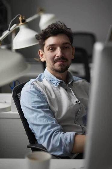 a man sitting in front of a laptop computer with his arms folded out and looking at the camera