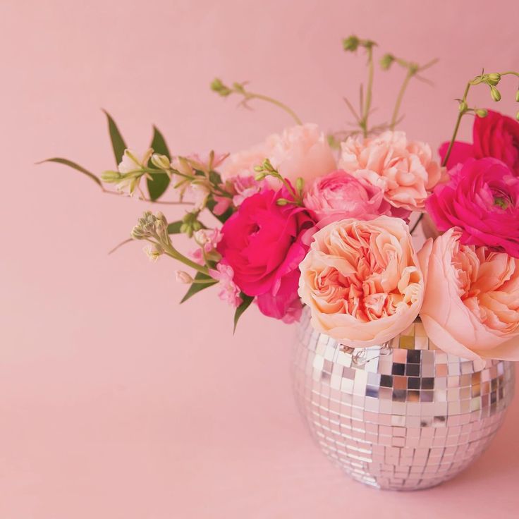 a disco ball vase filled with pink and red flowers on a pink background in front of a mirror wall