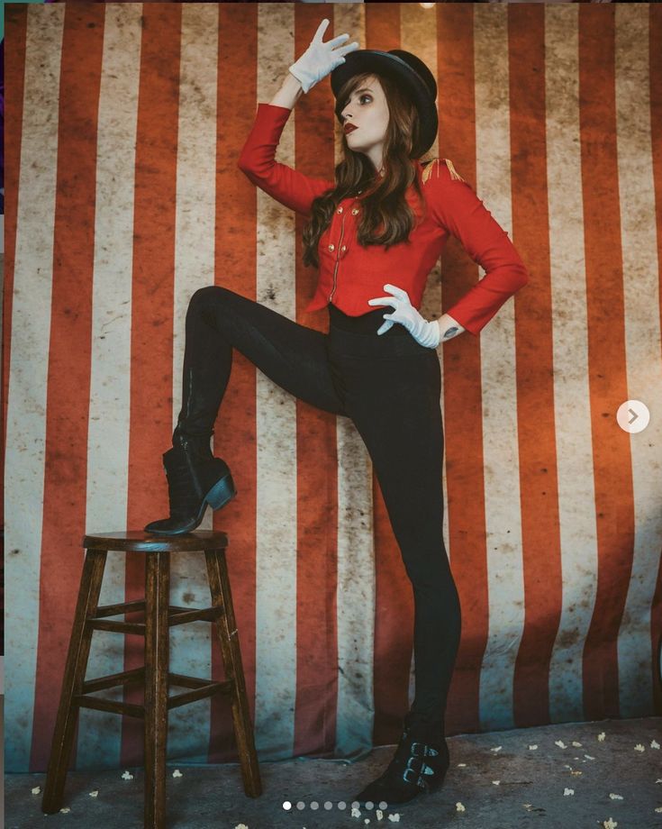 a woman in red shirt and black pants sitting on stool next to large striped wall