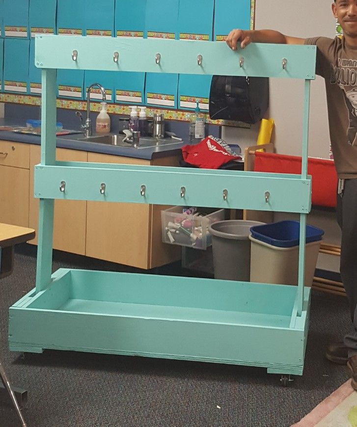 a man standing next to a blue shelf filled with bins and trash cans in a classroom