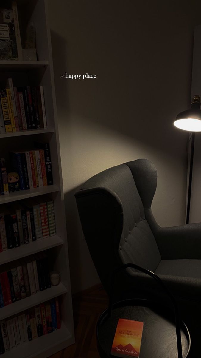 a living room with a chair, lamp and bookshelf in the background at night