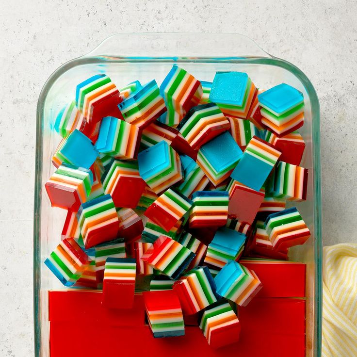 colorful candy cubes in a glass container next to a ball of yarn